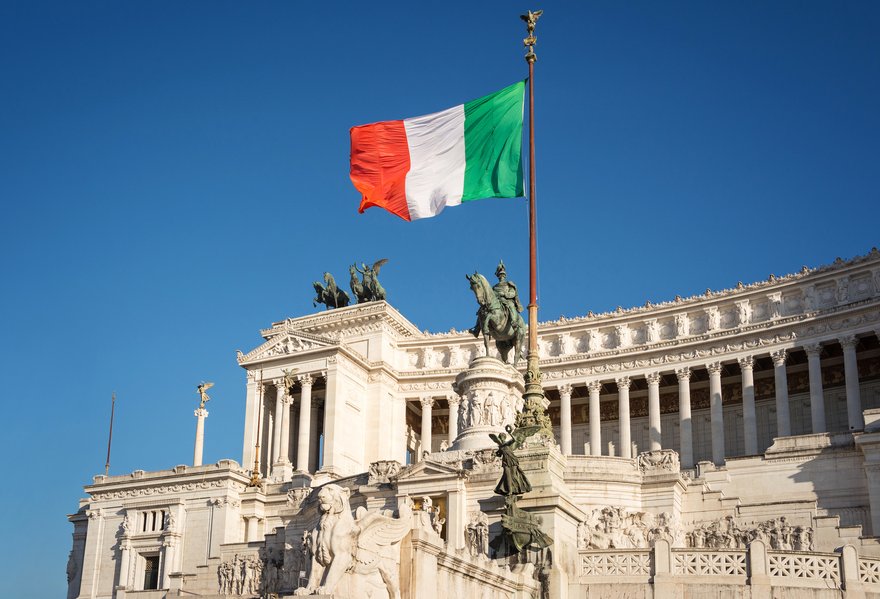 Bandera italiana con el rey Víctor Manuel II monumento ecuestre de fondo. Piazza Venezia, Roma, Italia.