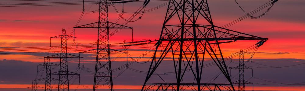 Dramatic sunset silhouette of towering electricity pylons against a vibrant orange and purple sky