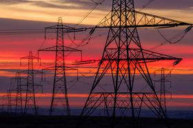 Dramatic sunset silhouette of towering electricity pylons against a vibrant orange and purple sky