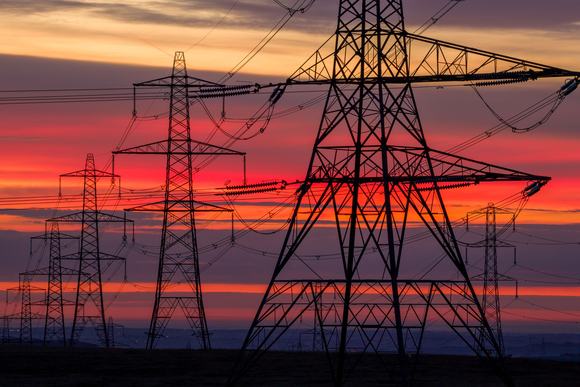 Dramatic sunset silhouette of towering electricity pylons against a vibrant orange and purple sky
