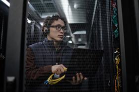 Person Working with Laptop and Network Cables in Server Room